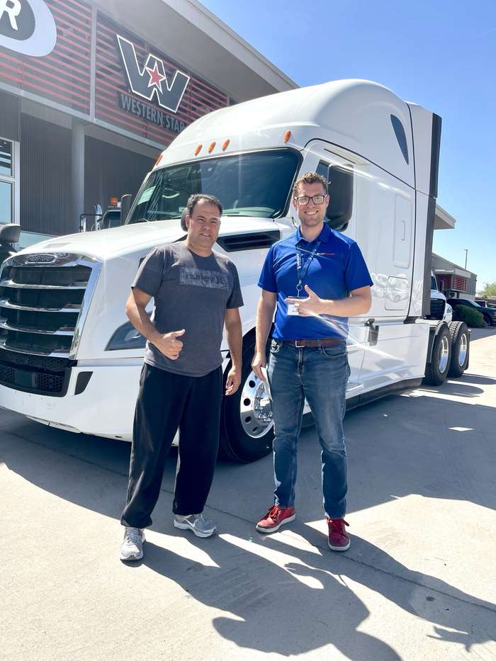 Rob standing with a happy customer in front of a white Freightliner Cascadia at pickup time at the dealership