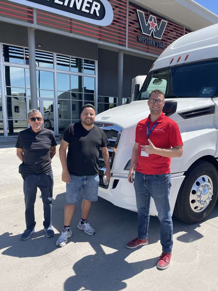 Rob with two happy customers in front of a white truck at the dealership